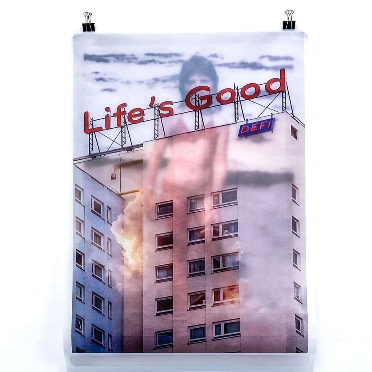 Life's Good : tirage suspendu, une tour d'habitation surmontée d'une enseigne Life's Good et d'un panneau DEFI, une silhouette d'enfant en surimpression dans le ciel
